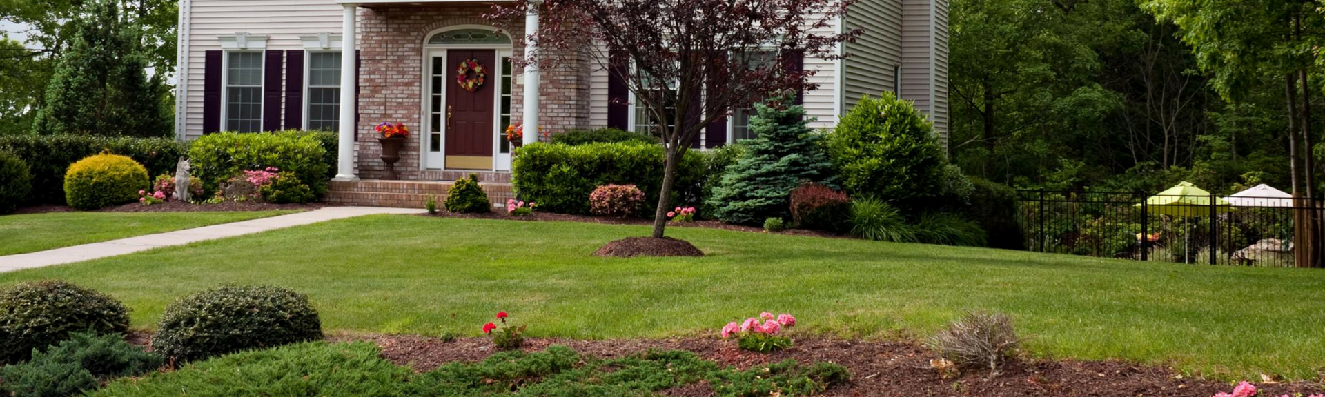 Suburban house with a red front door, landscaped lawn, and trimmed bushes in the yard.