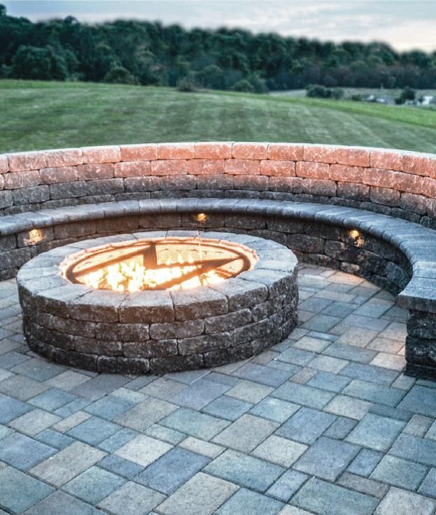 Stone fire pit with glowing flames in a curved brick seating area on a patio at dusk