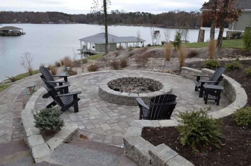 Stone fire pit patio with black chairs overlooking a calm lakeside dock and cloudy water