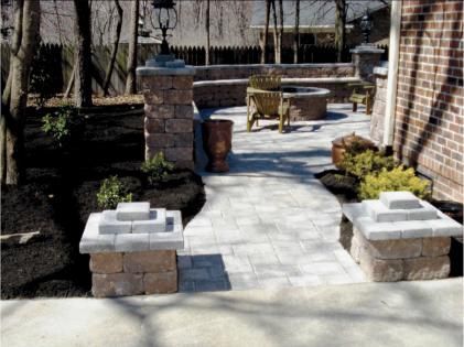 Brick patio walkway with low stone planters leading to a backyard seating area