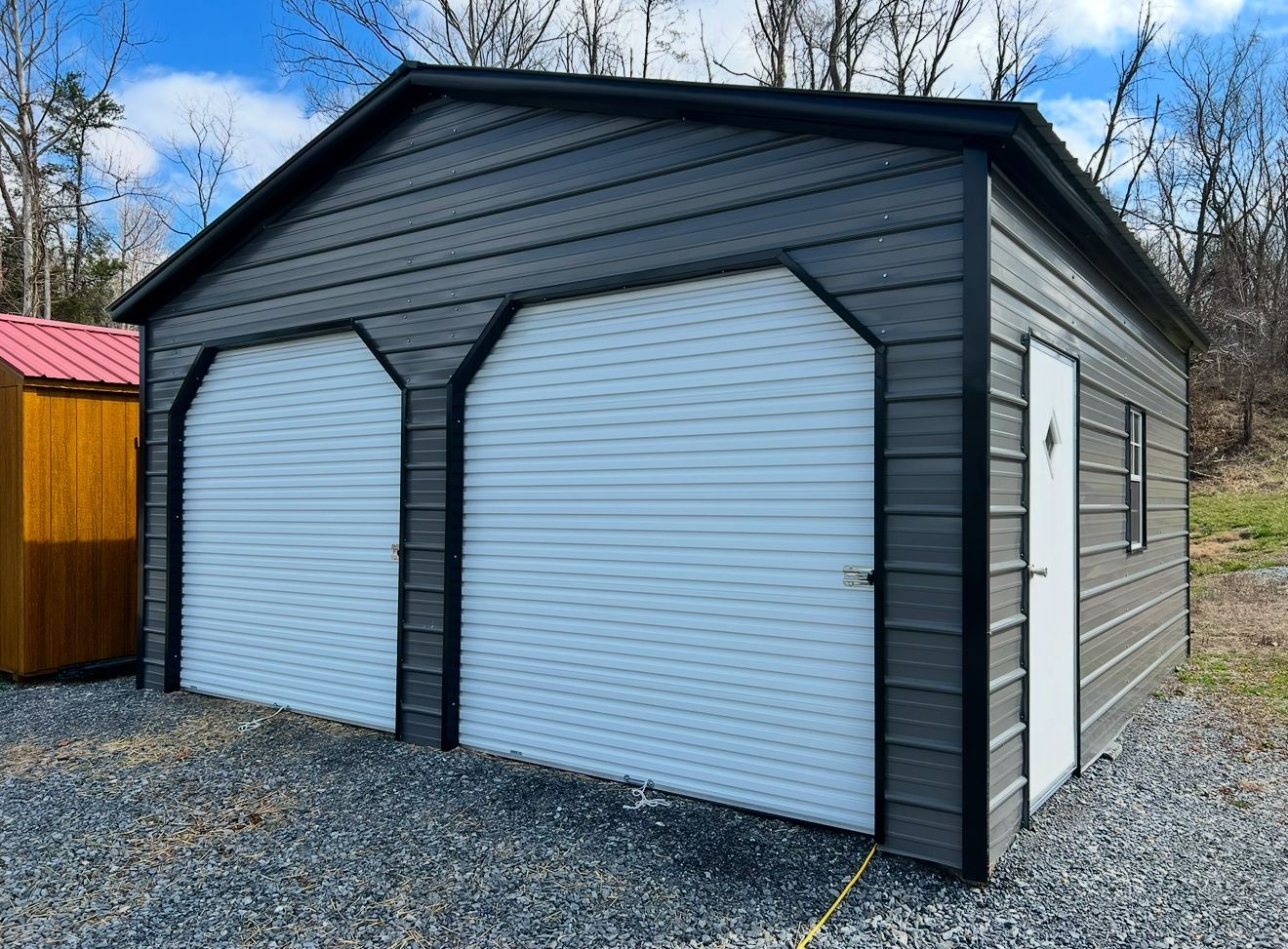 Double garage with black trim and two white roll-up doors on a gravel driveway