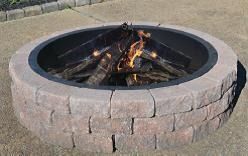 Stone fire pit with burning logs and small flames outdoors