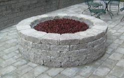 Round stone fire pit filled with red rocks on a paved patio