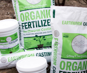 Green and white bags and jars of organic fertilizer and earthworm castings on a wooden surface