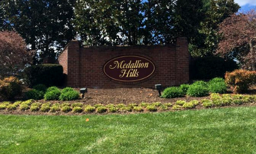 Brick entrance sign for “McMillin Hills” surrounded by landscaped shrubs and grass under trees