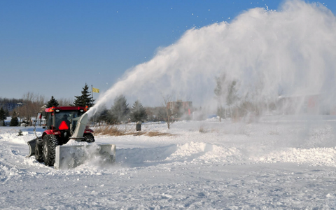 Snowblower clearing deep snow in a snowy field, spraying a large plume into the air.