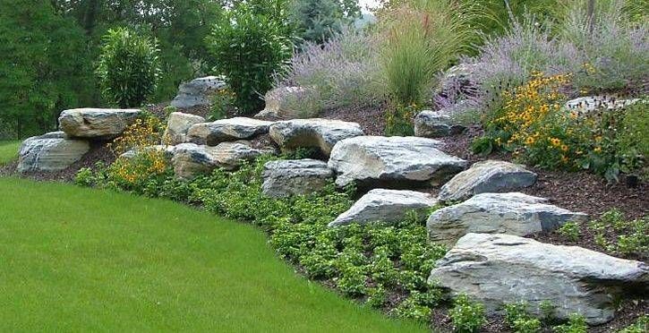 Rock garden with large white stones, green lawn, and flowering shrubs along a landscaped slope