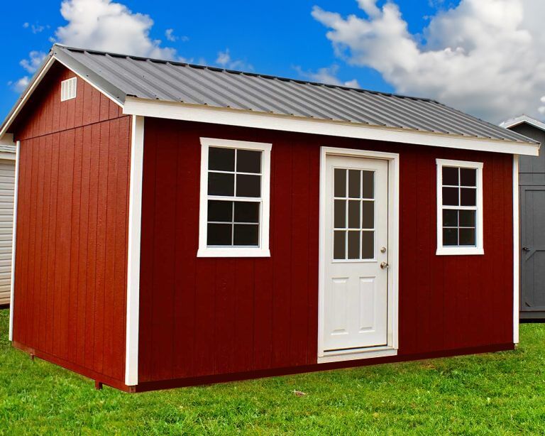 Red shed with white trim, two windows, and a white door on a grassy lawn under a cloudy sky