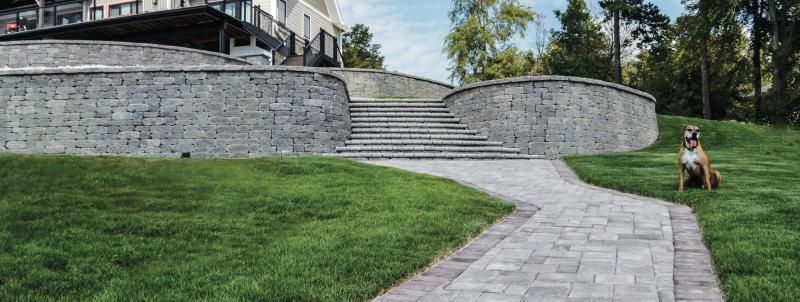 Curved stone wall and stairs beside a grassy path, with a dog sitting on the right.