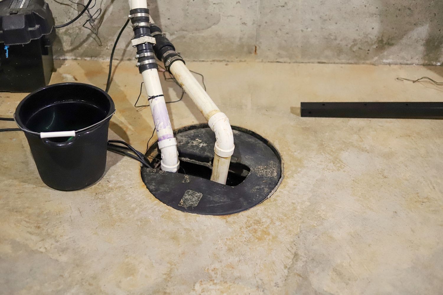 A bucket of water is sitting next to a sump pump in a basement. Sump pump in basement