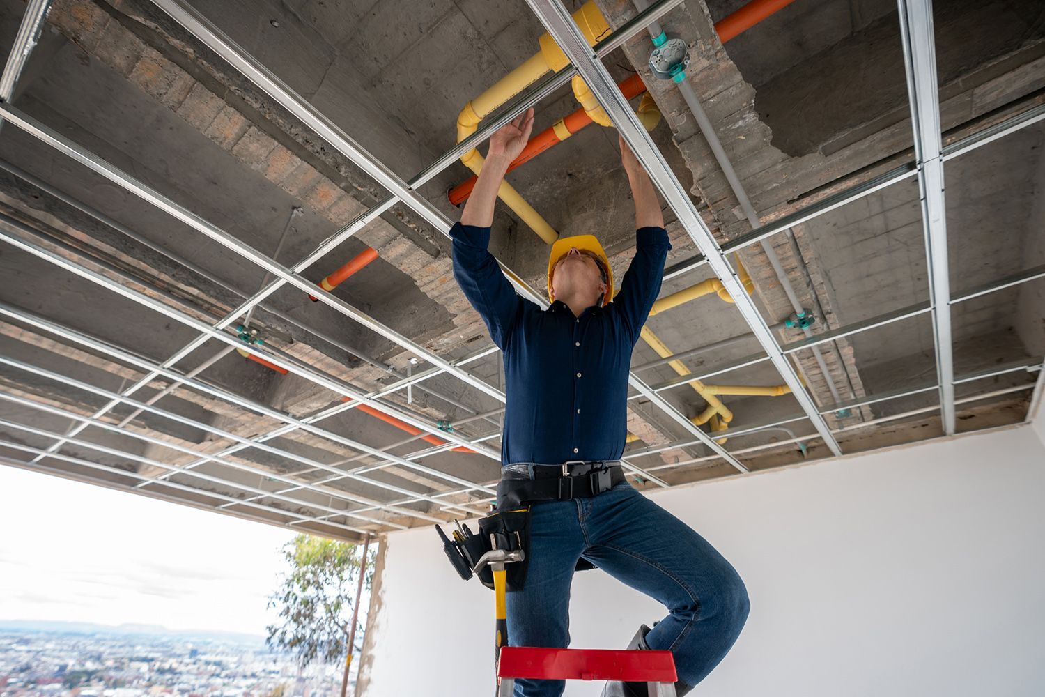 A man is standing on a ladder working on a ceiling.