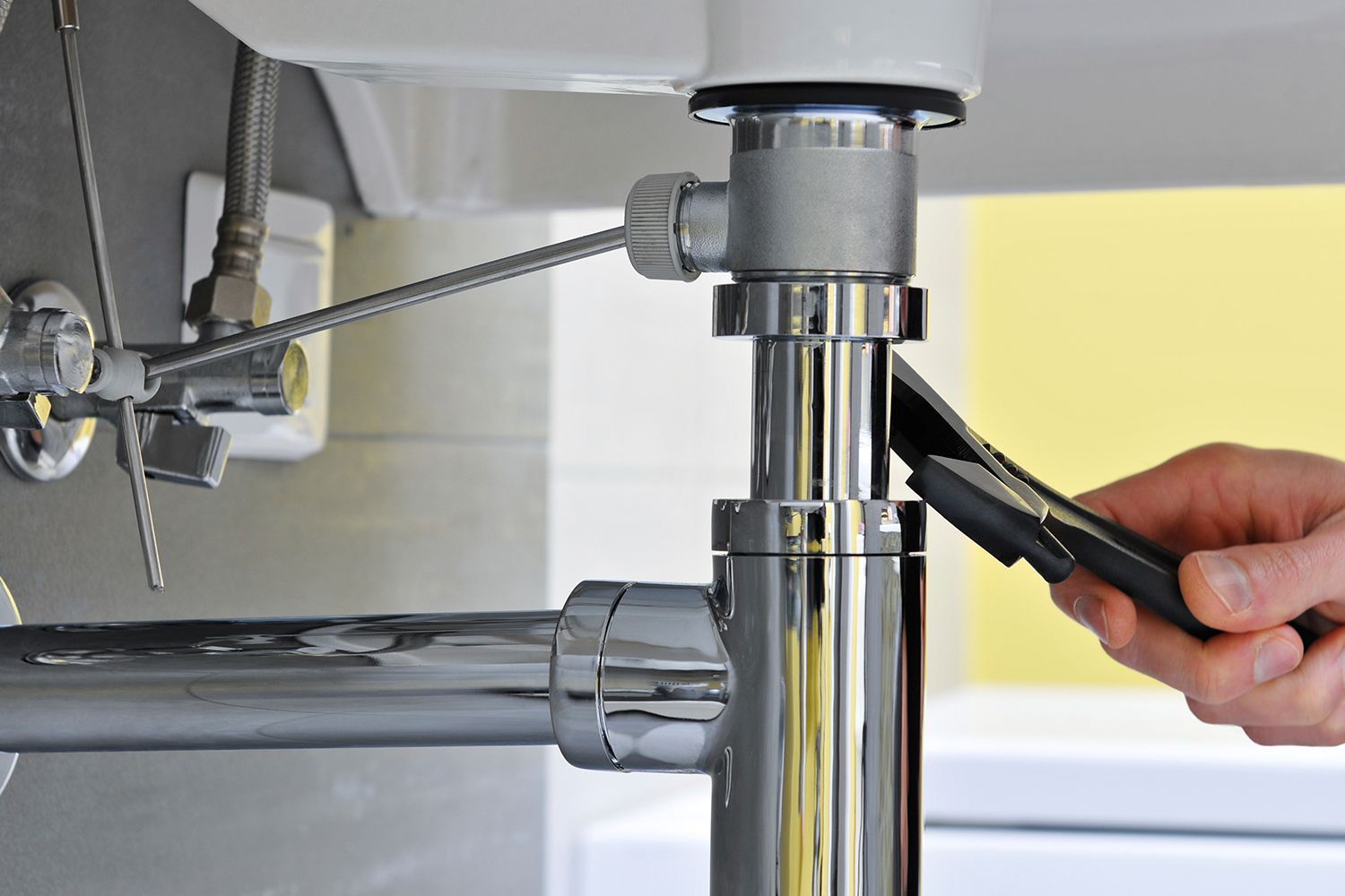 A person is fixing a sink pipe with a wrench. A person is fixing a sink pipe with a wrench.