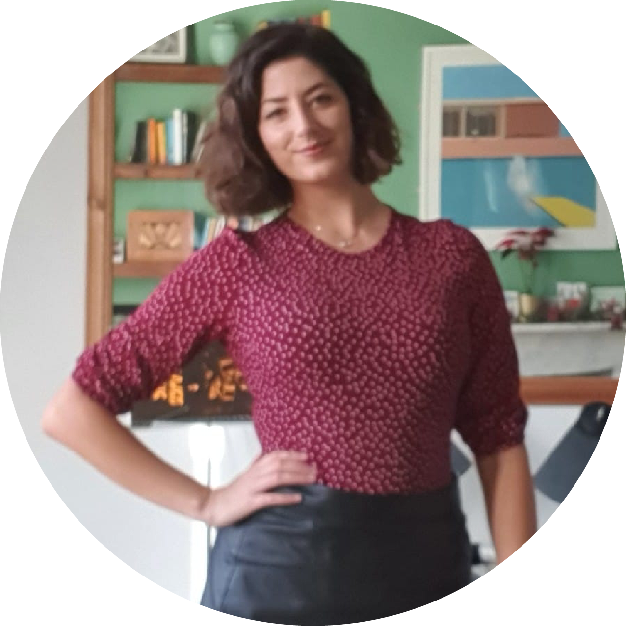 A woman in a maroon top and black skirt stands with her hand on her hip