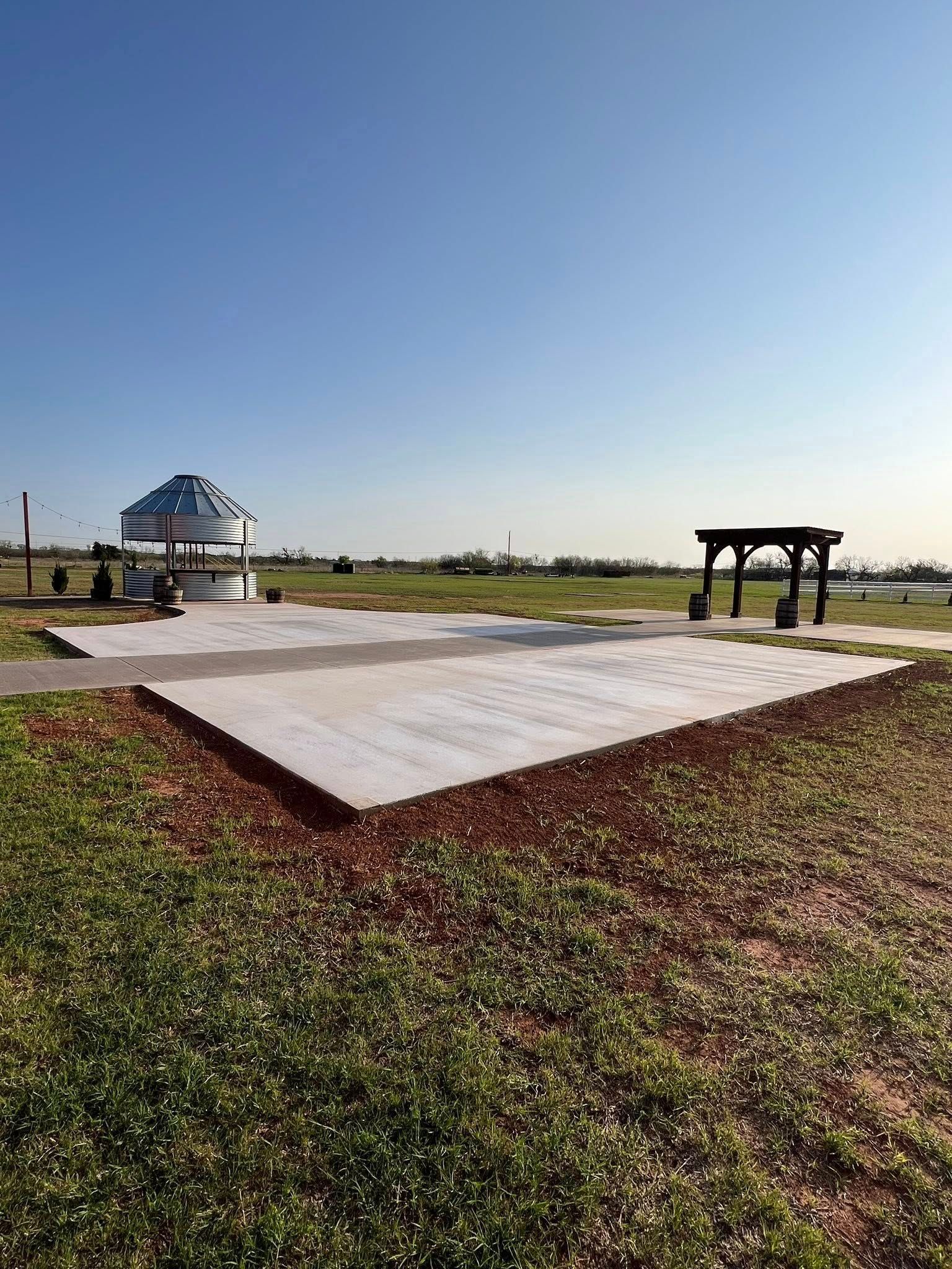 An outdoor space with a concrete slab, wooden shelter, and sculpture under a blue sky.