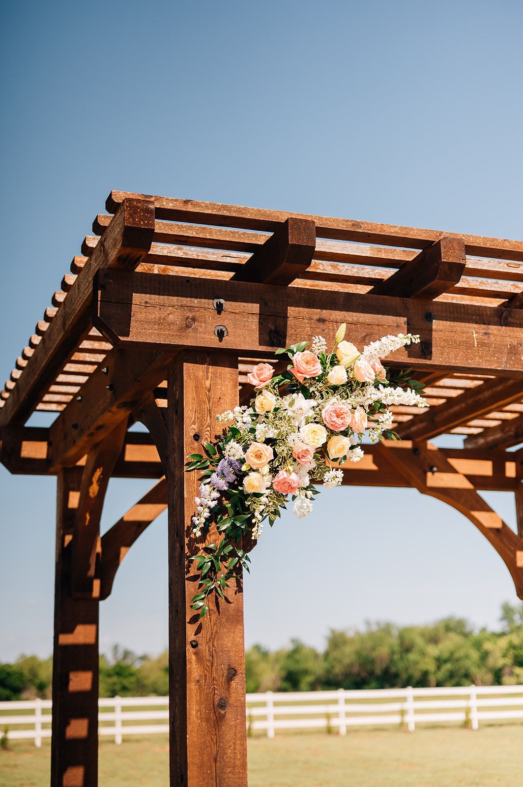 Wooden arbor decorated with pastel flowers against a clear blue sky.