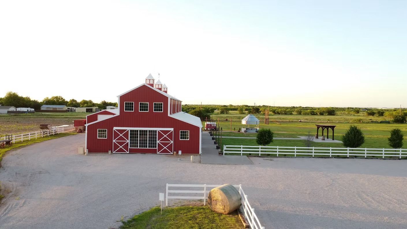 Red barn with white trim, set on a gravel driveway, in a field, under a clear sky.