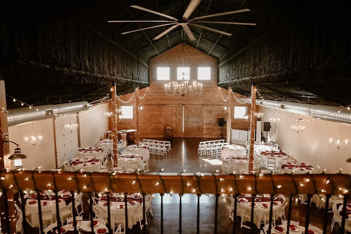 Wedding reception hall with tables set for guests, rustic decor, and overhead lighting.