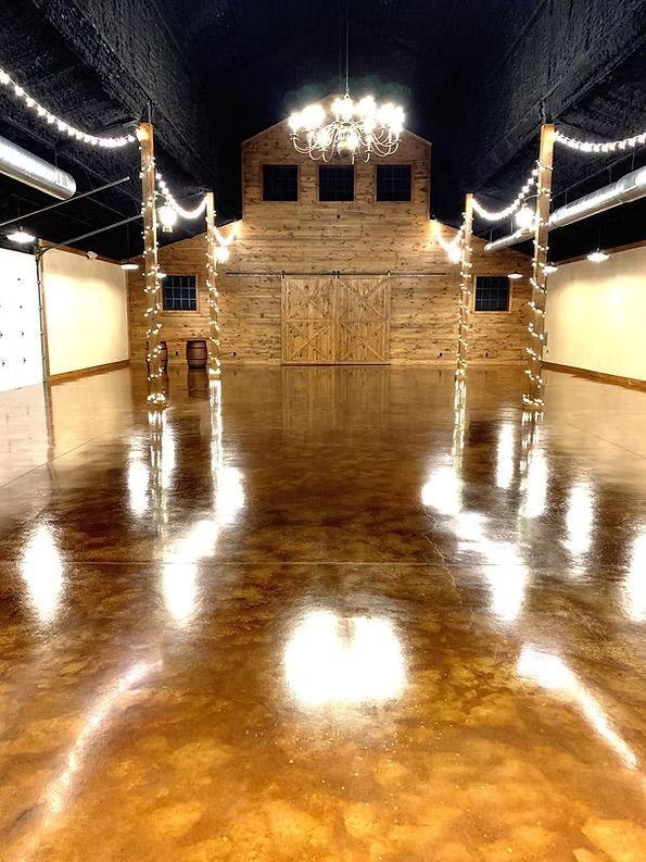 Empty barn interior with polished brown floor, wood-paneled wall, and string lights.