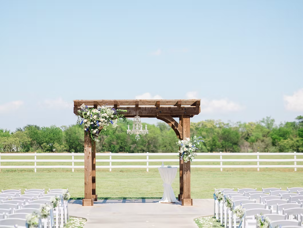 Wedding ceremony arch with floral arrangements and chandelier, outdoor setting.