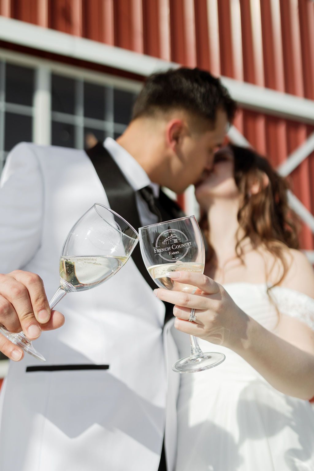 Couple embracing at a wedding, leaning on a white fence, with a windmill in the background.