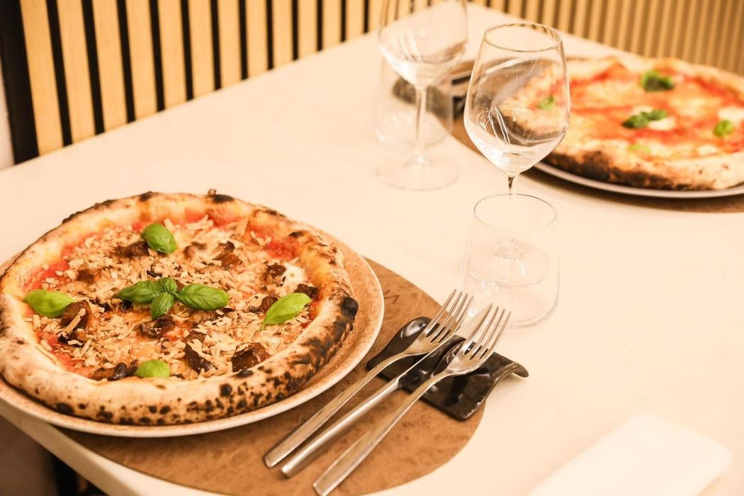 Due pizze su un tavolo di ristorante con bicchieri da vino e posate.