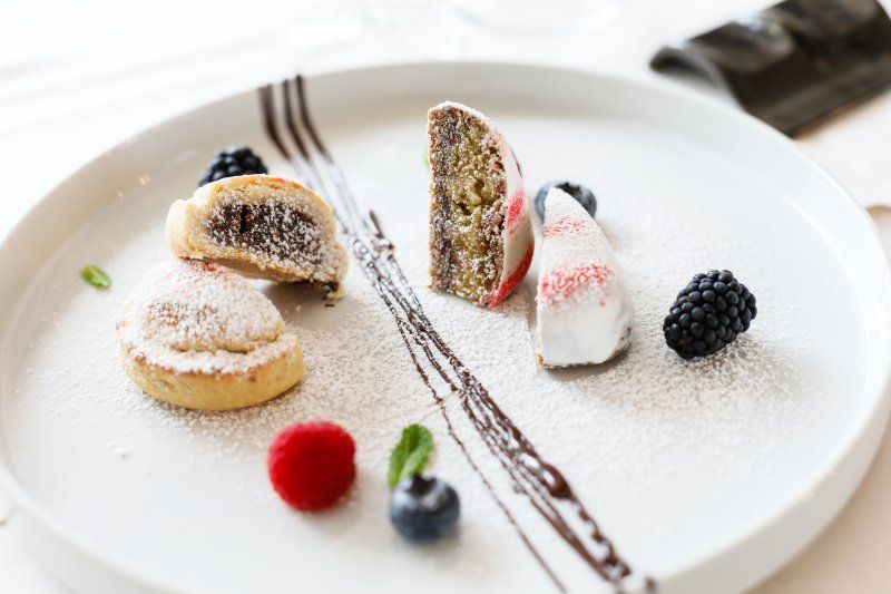 Assortimento di dessert al piatto con zucchero a velo, frutti di bosco, glassa al cioccolato e decorazioni di panna.