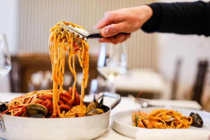 Piatto gourmet impiattato con verdure colorate su un tavolo bianco in un ambiente di ristorante.