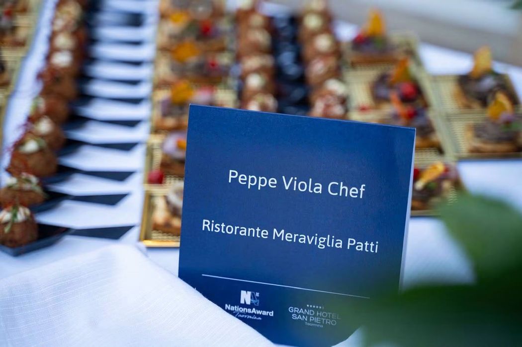 Terrazza esterna del ristorante con tavoli con tovaglie bianche, sedie nere e cuscini turchesi.