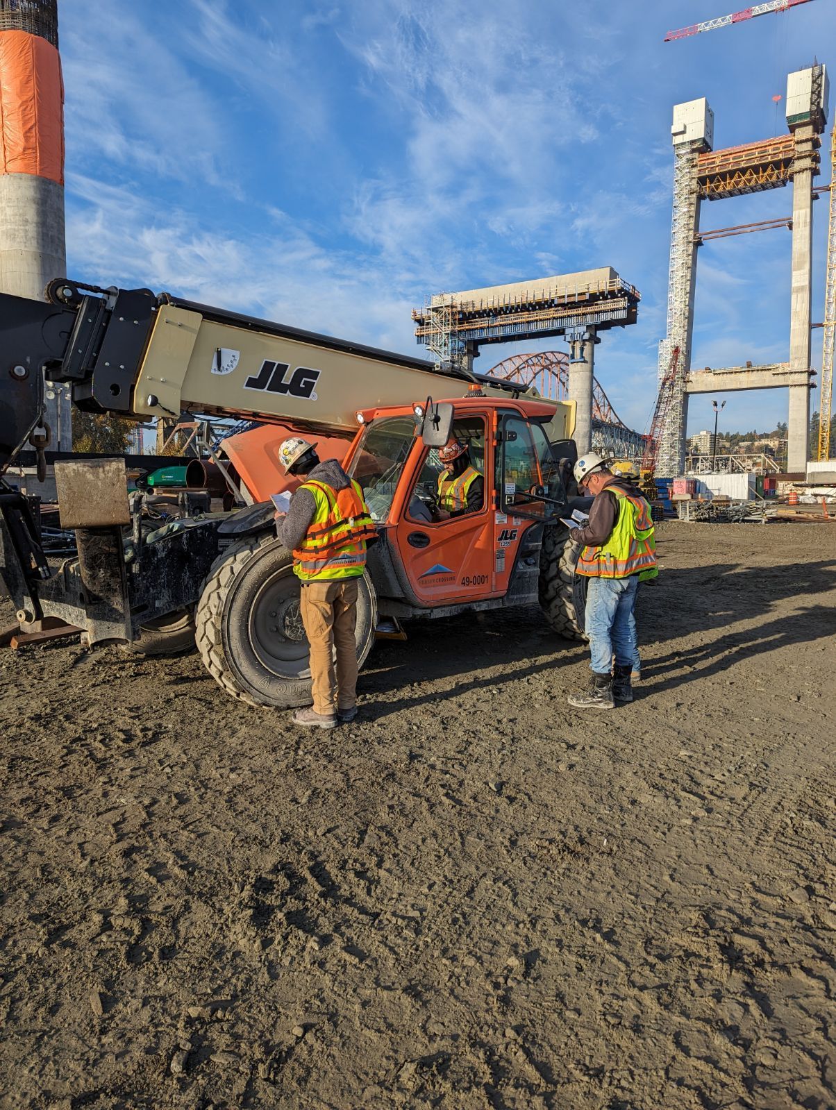 A group of construction workers are standing next to a forklift on a construction site. 