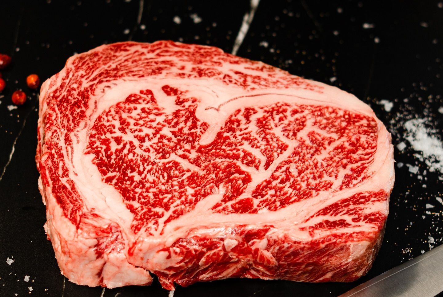 Raw marbled ribeye steak on a dark skillet, red and white fat streaks visible