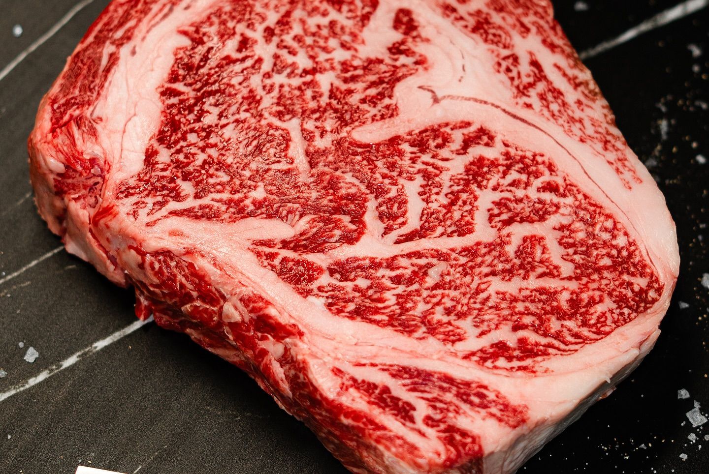 Raw marbled ribeye steak on a dark cutting board with coarse salt