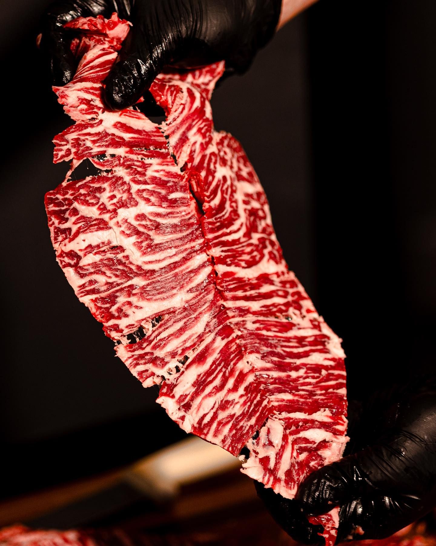 Gloved hands holding a marbled raw steak against a dark background