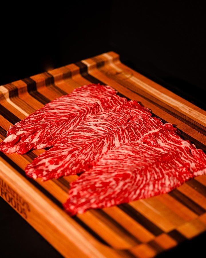 Thinly sliced marbled raw beef on a striped wooden cutting board against a dark background