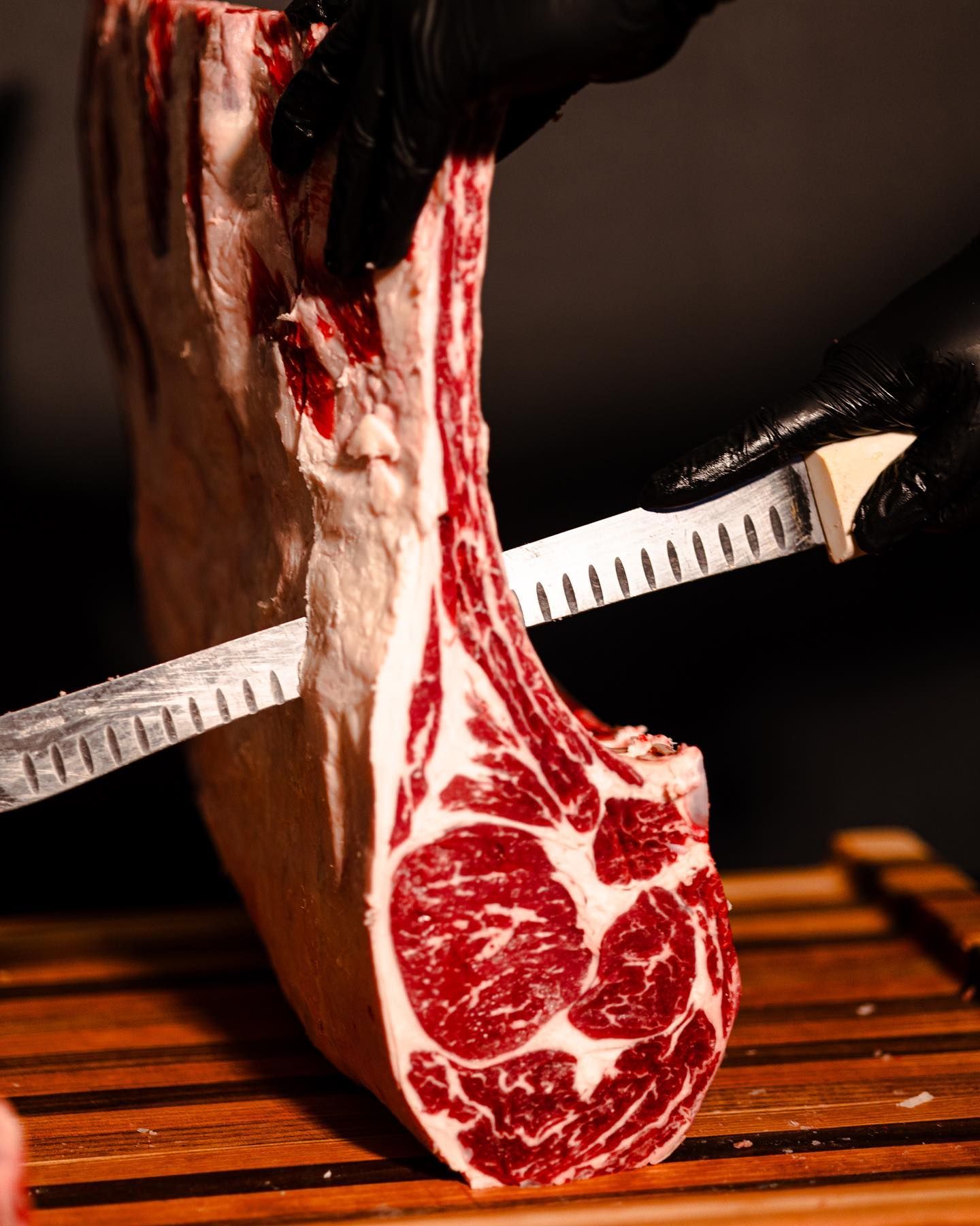 Raw marbled steak being sliced with a knife on a wooden cutting board