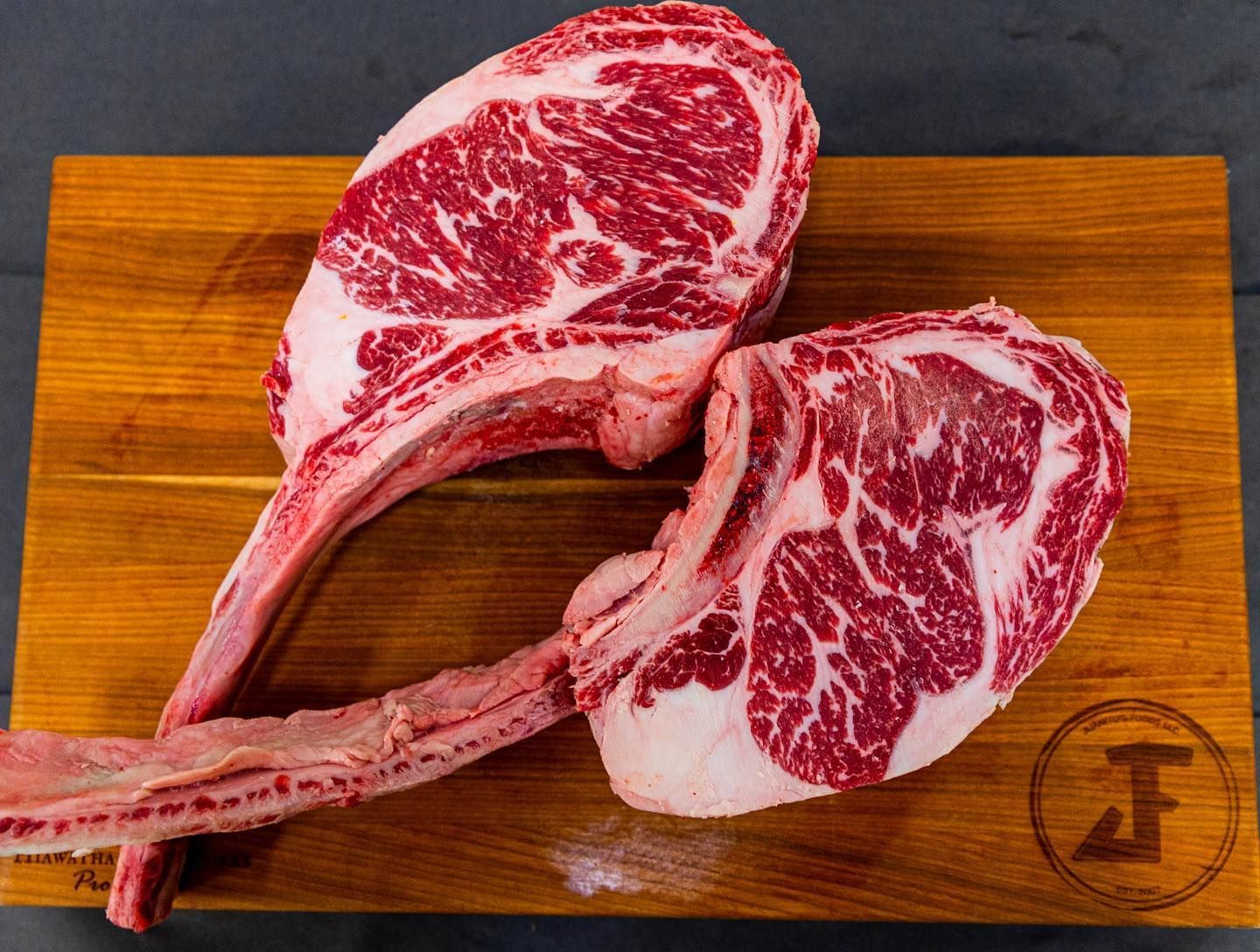 Two raw tomahawk steaks on a wooden cutting board, marbled red meat with long bone handles