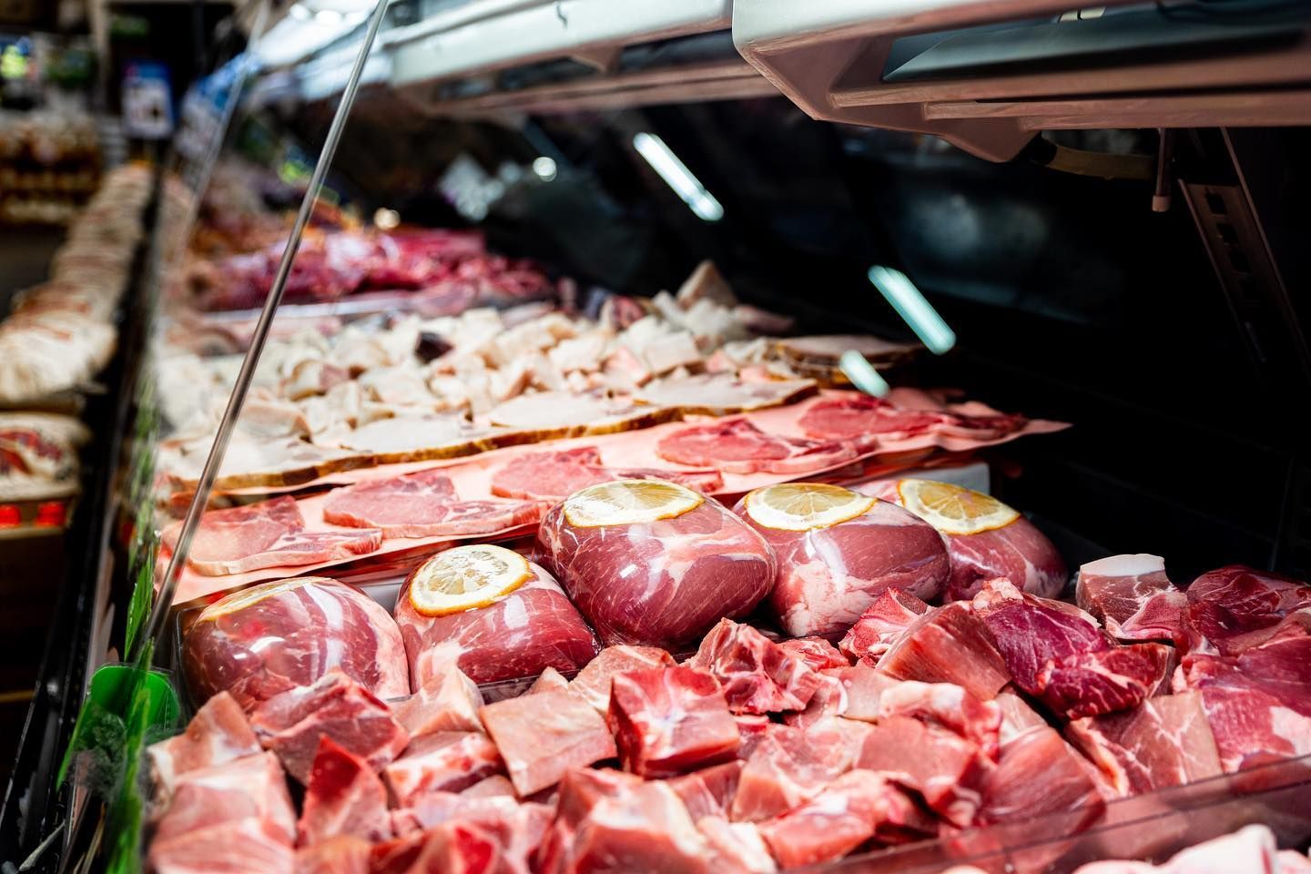 Display of assorted raw meats at a butcher counter, including red cuts and wrapped pieces