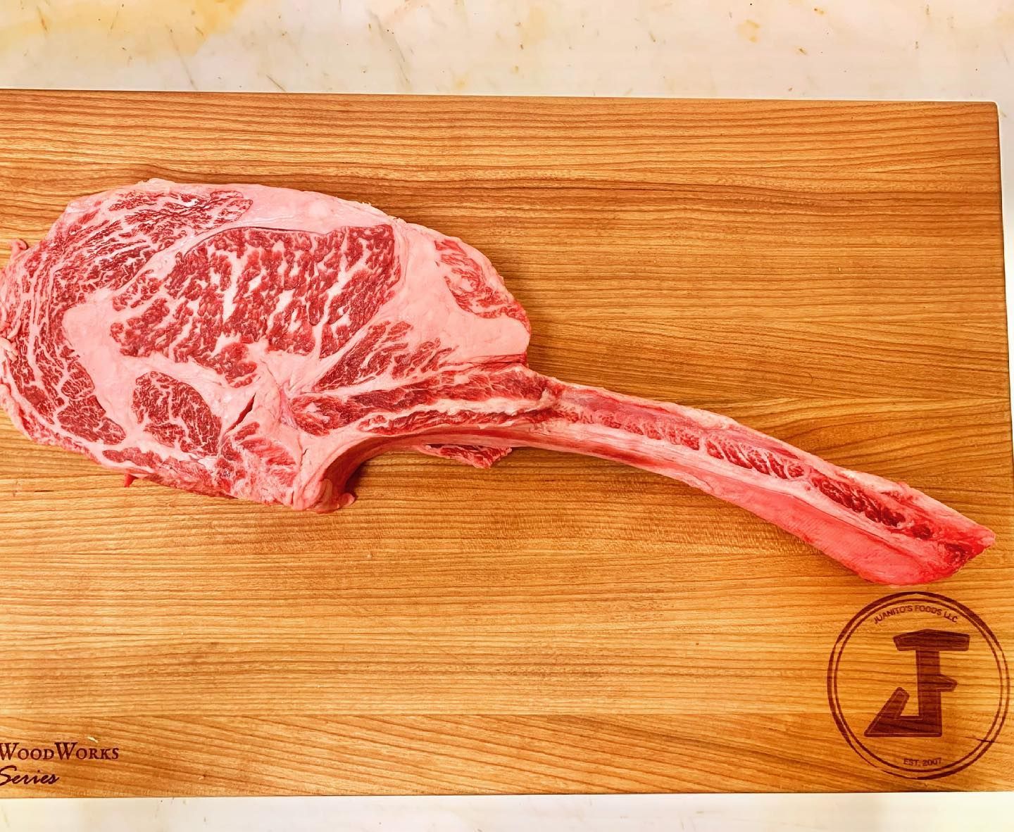 Marbled raw tomahawk steak on a wooden cutting board, with long bone attached