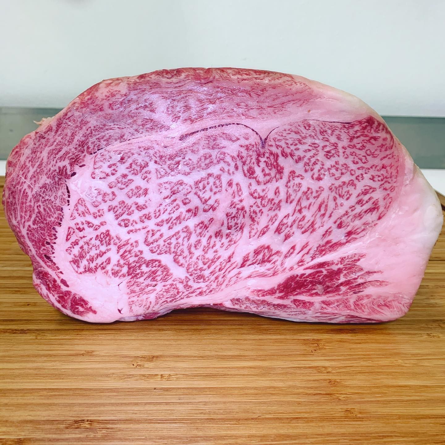 Marbled raw beef steak on a wooden cutting board against a light background
