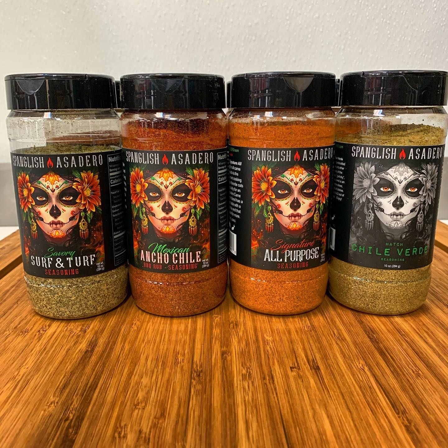 Four spice jars on a wooden table, labeled Witch’s Brew, Magic Cobbler, All-Purpose, and one black blend.