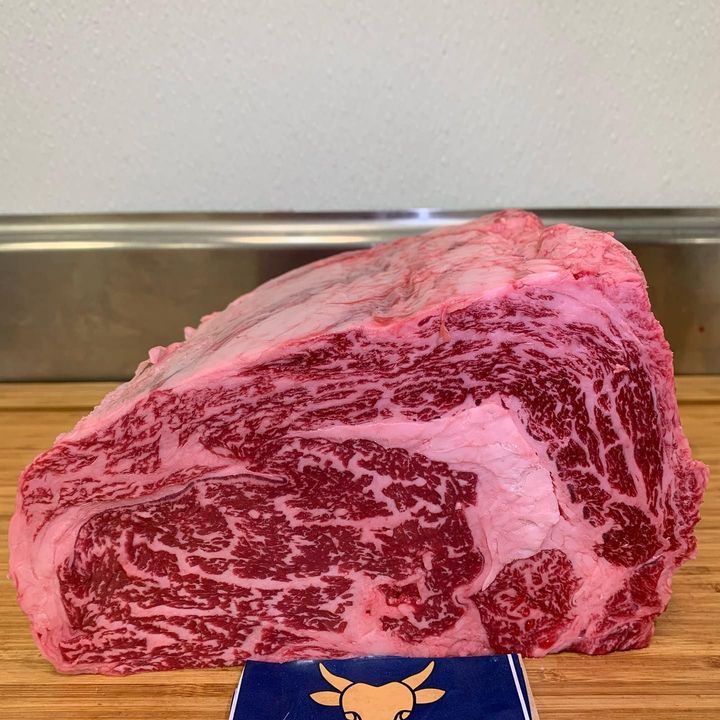 Marbled raw beef steak on a cutting board, with a blue tag in front