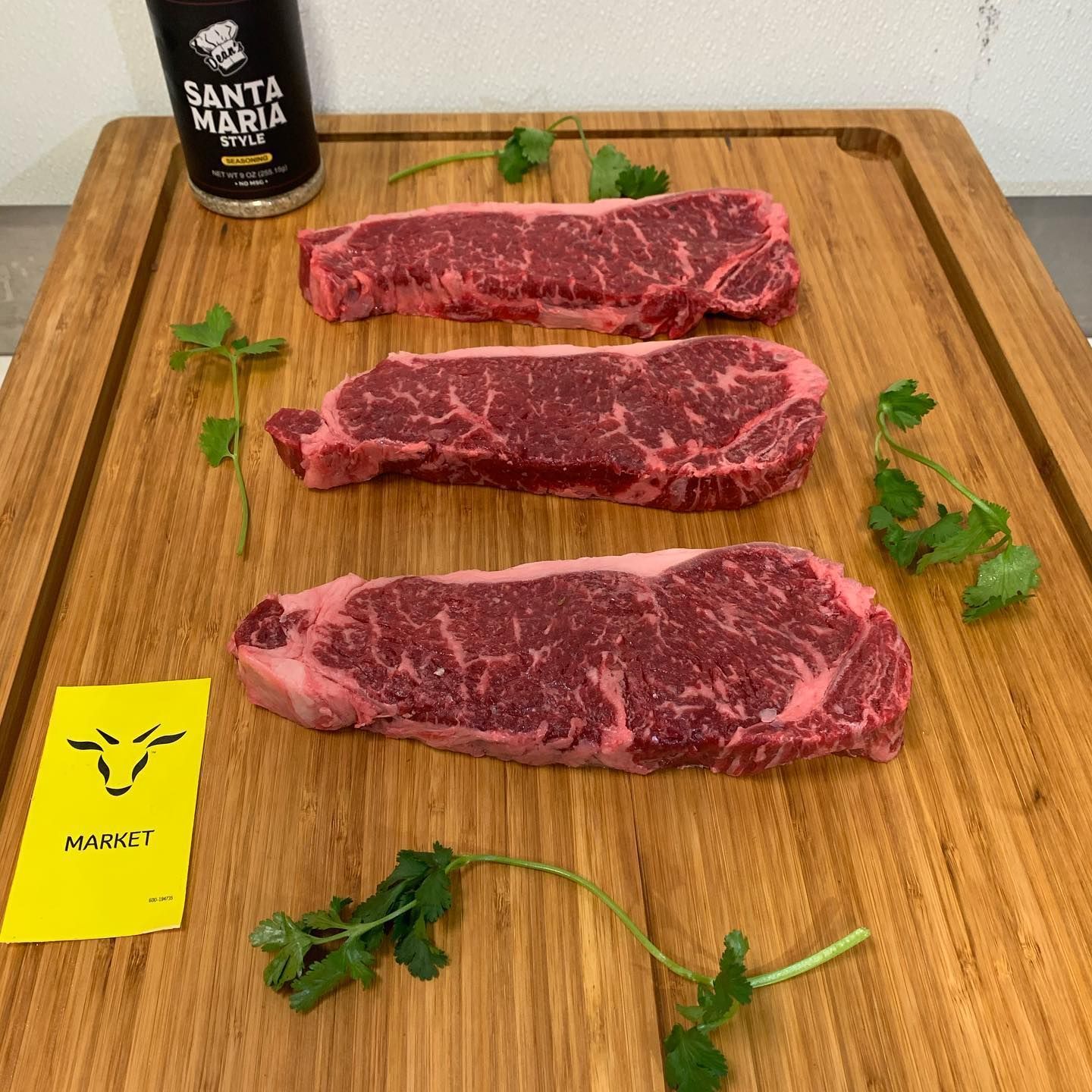 Three raw marbled steaks on a wooden board with parsley and a Santa Maria bottle.