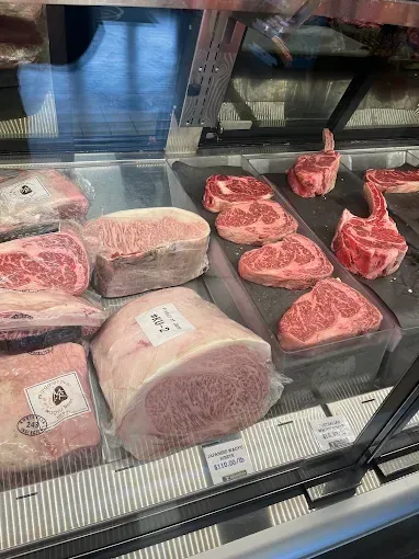 Display case with assorted raw beef cuts and steaks in a butcher shop.