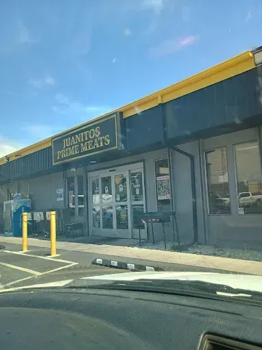 Storefront of a vacant retail building with dark windows, yellow bollards, and a blue sky overhead