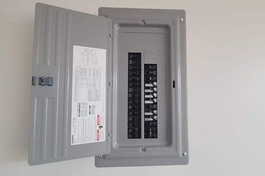 Open electrical breaker panel with gray cover on a white wall