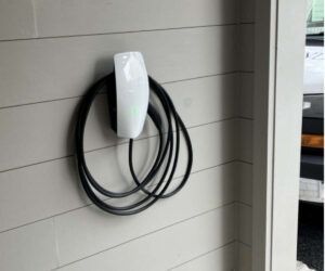 White EV charger mounted on a wall with a black charging cable coiled around it