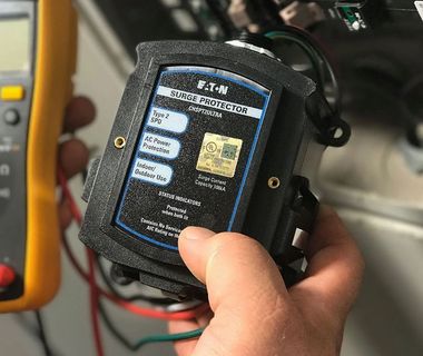 Hand holding a black Eaton diagnostic device with a color display and cables attached in a workshop.