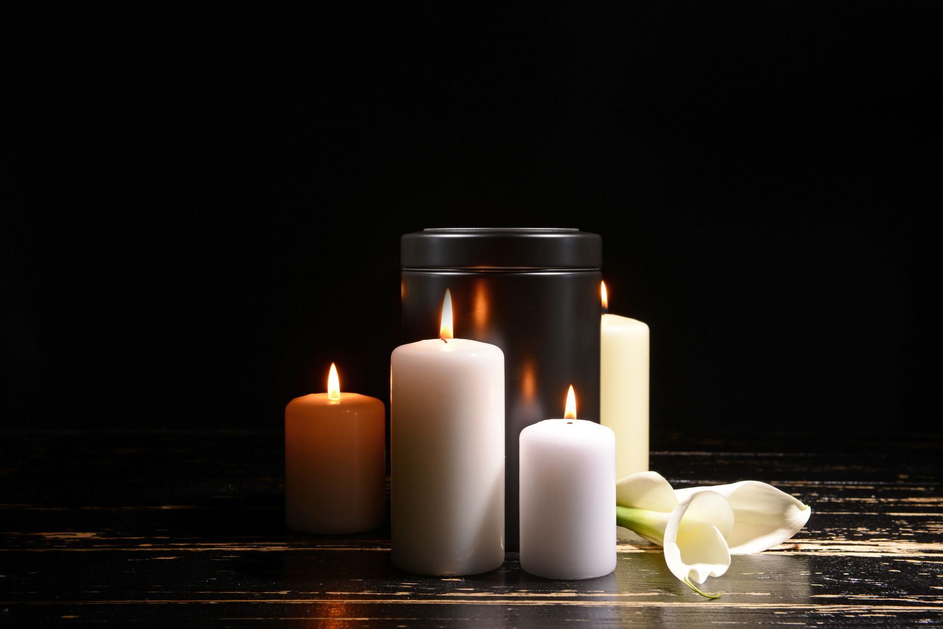 Lit white and orange candles with white flowers on a dark reflective surface
