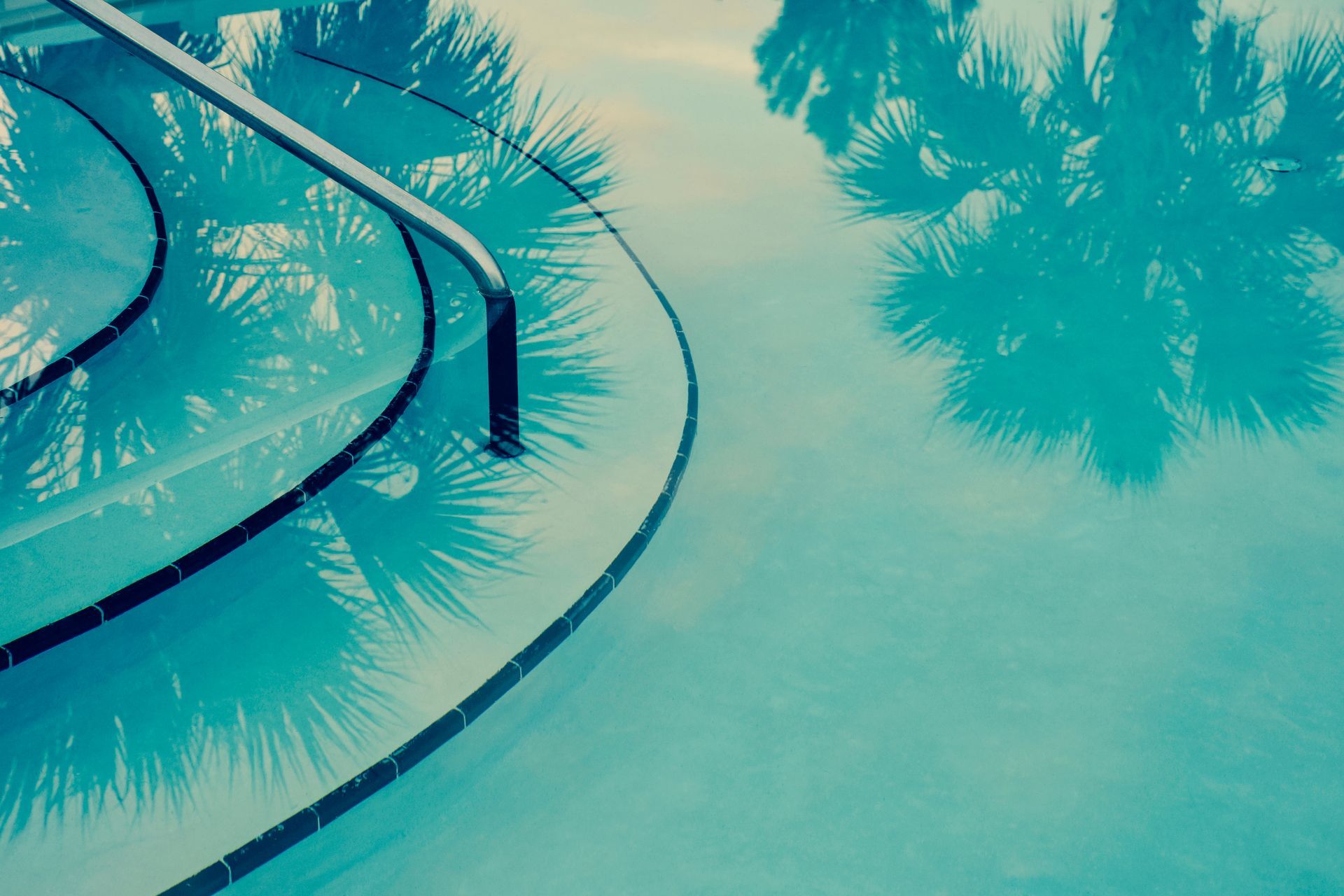 A serene pool surrounded by palm trees, featuring a staircase leading into the water.