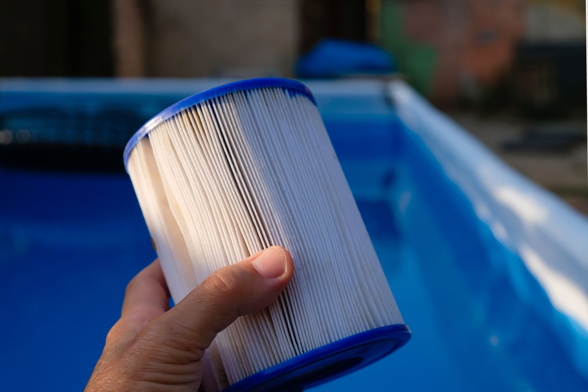A person is holding a filter in front of a swimming pool.