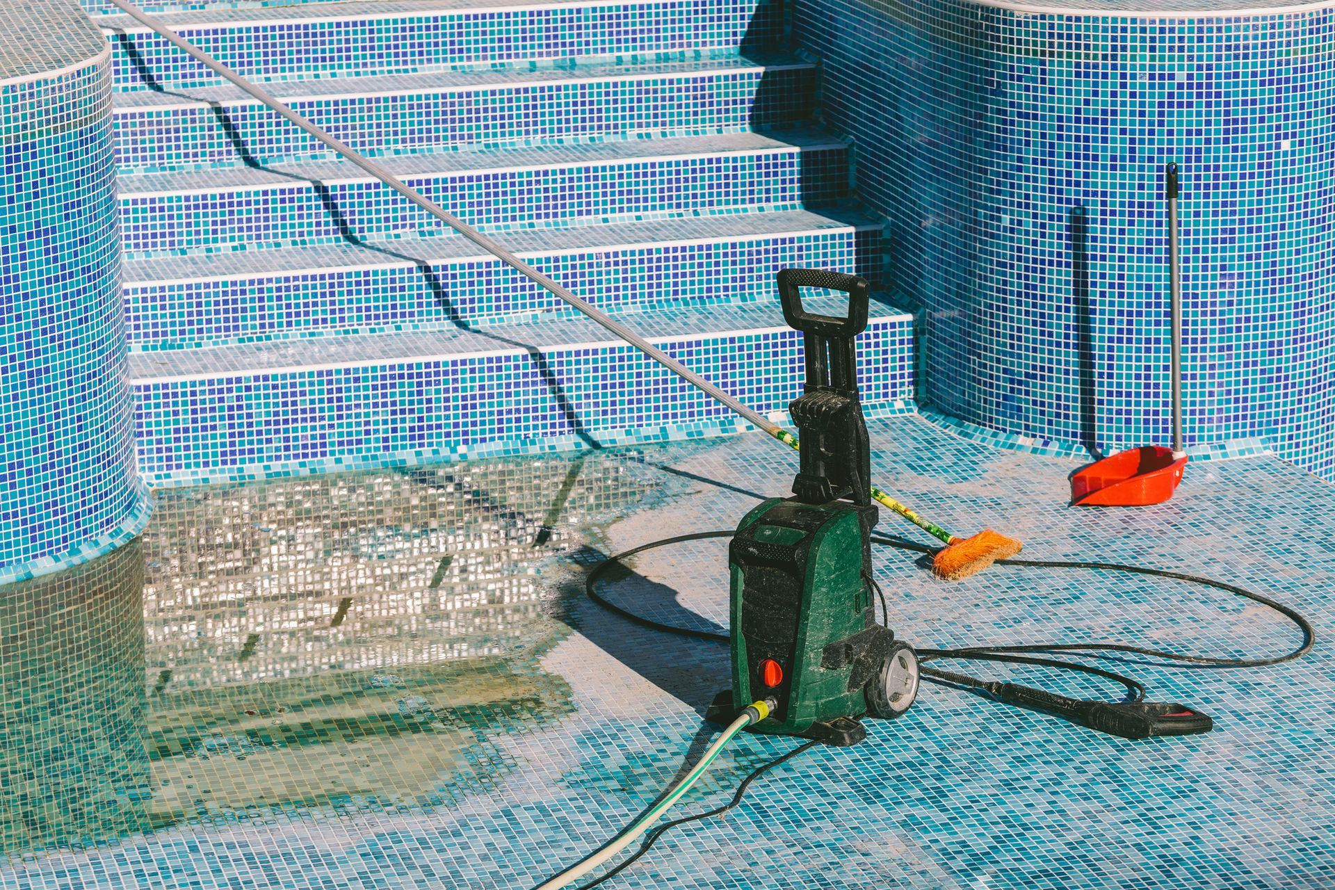 A high pressure washer is sitting on the ground next to a swimming pool.